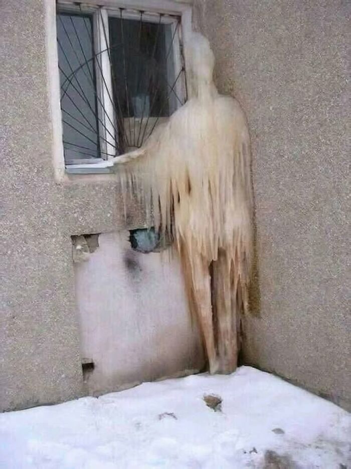 Bizarre ice formation resembling a figure by a window on a snowy day.