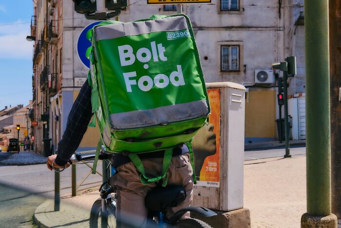 Delivery rider with a large green Bolt Food backpack cycling on a city street.
