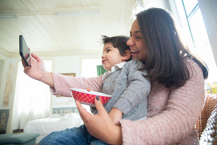 Mom smiling with toddler, taking a selfie in a cozy room, highlighting family bond despite non-talkative behavior concerns. Mom smiling with toddler, taking a selfie in a cozy room, highlighting family bond despite non-talkative behavior concerns.