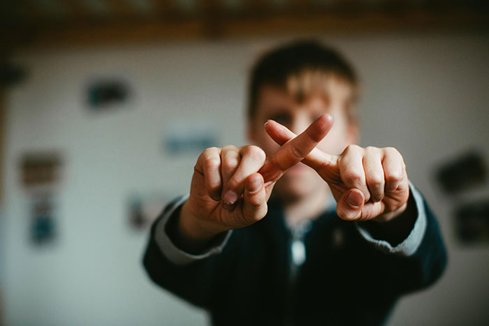 A child in a dimly lit room, crossing fingers to make an "X" gesture, representing non-talkative behavior concerns. A child in a dimly lit room, crossing fingers to make an "X" gesture, representing non-talkative behavior concerns.
