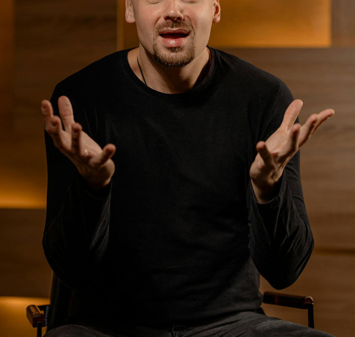 Man in a black shirt gesturing with open hands, discussing hysterectomy and surrogacy pressures. Man in a black shirt gesturing with open hands, discussing hysterectomy and surrogacy pressures.