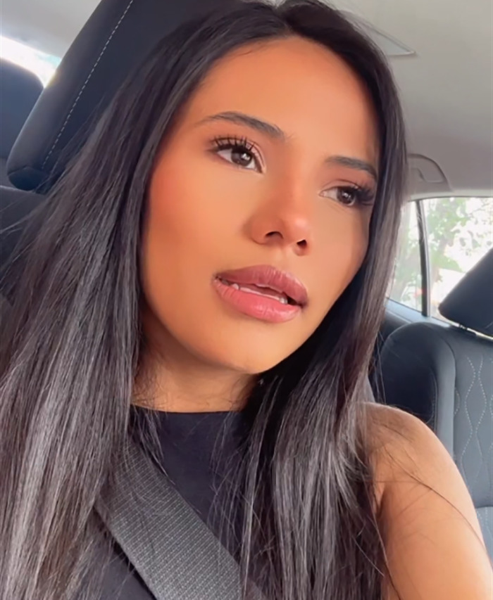 Woman in a car, contemplating after discovering dating profile truth, wearing a black top and seatbelt.