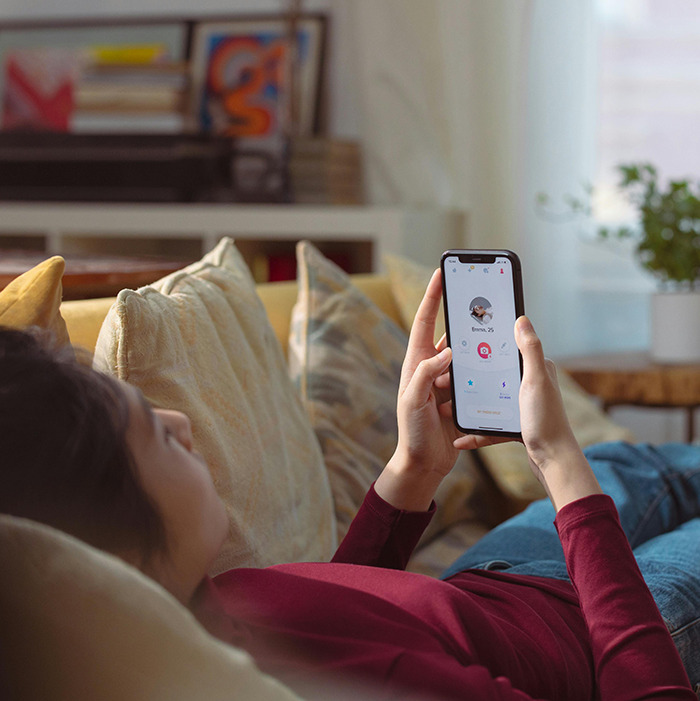 Woman using a dating app on her phone while lying on a couch, exploring dating profiles.