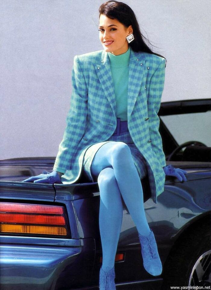 80s fashion trends: Woman in blue plaid blazer and matching tights sitting on a car.