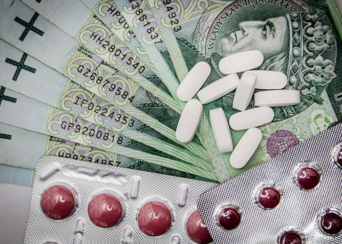 White pills and blisters of red tablets placed on various currency notes, highlighting American healthcare issues.