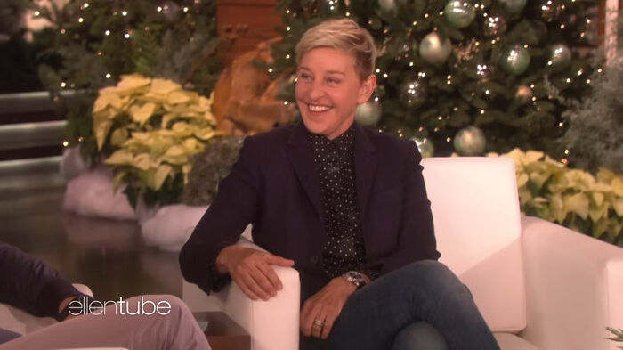 Comedian smiling on a talk show set with festive decorations.