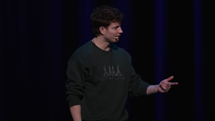 Comedian on stage with a black shirt, performing under spotlight, discussing mainstream transition.
