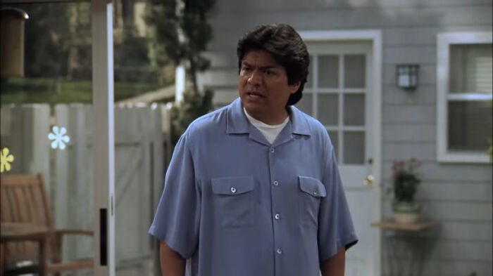 A man in a blue shirt stands in a backyard, looking concerned. Mainstream comedian moment captured.