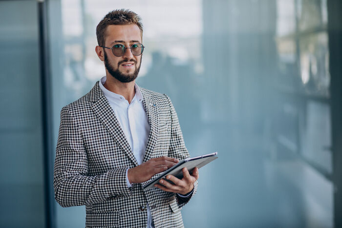 Man in a checkered blazer with a tablet, symbolizing high-paying remote jobs, standing in a modern office setting.