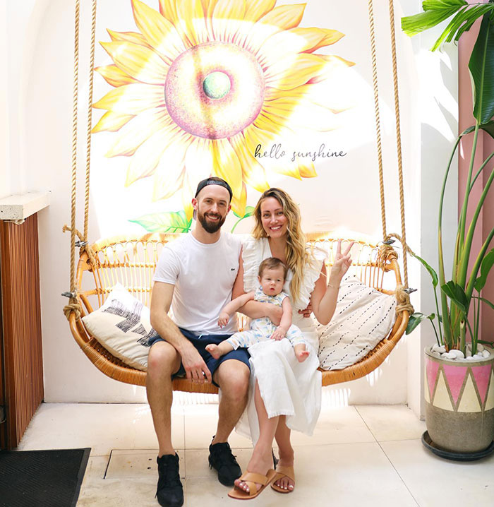 Family sitting on a swing, smiling, with a sunflower mural and the text "hello sunshine" in the background.