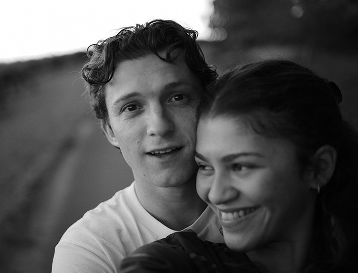 Tom Holland smiling outdoors, embracing Zendaya in a casual setting.