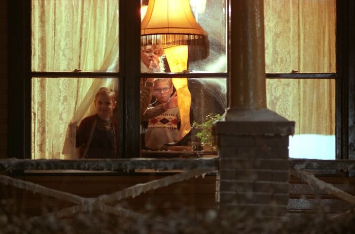 Children looking outside through a window with a famous movie prop, the leg lamp, glowing warmly beside them.
