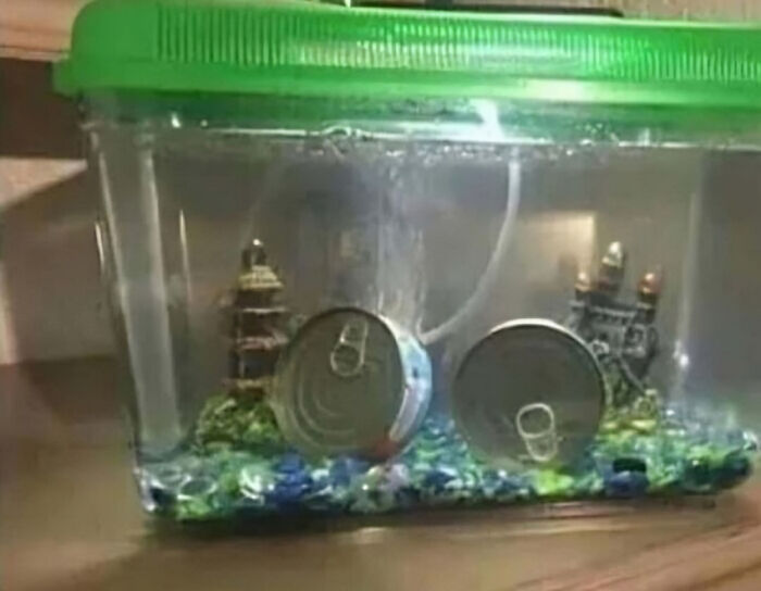 Two sealed cans submerged in a fish tank, surrounded by colorful gravel and small decorative structures.