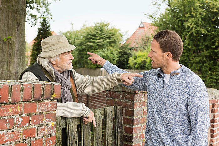 Neighbors arguing outside near a brick fence about light complaints.