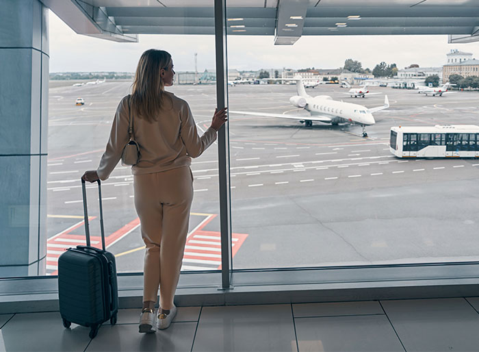 Woman with luggage at airport terminal, gazing at plane outside the window. Woman with luggage at airport terminal, gazing at plane outside the window.