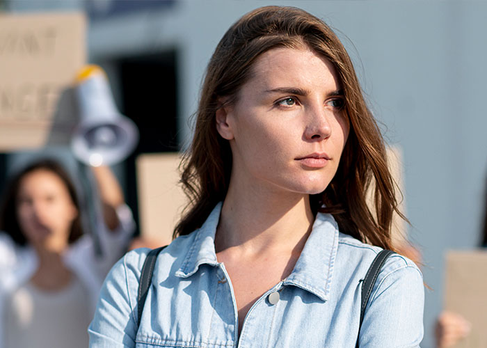 Woman looks serious, standing outside with protest signs visible, highlighting a Planned Parenthood visit for cancer screening.