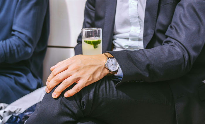 Man in suit holding a cocktail, seated, highlighting "coworkers' game" context, and wearing a wristwatch.