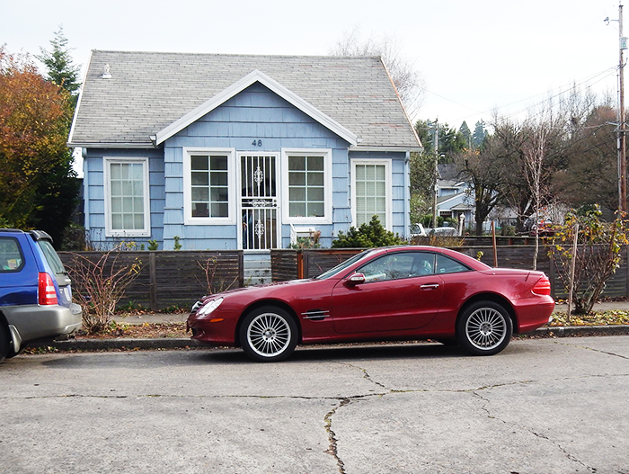 Red car parked in front of a blue house illustrating parking revenge on a thoughtless neighbor.