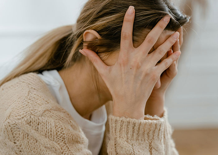 Woman in distress, hands covering face, wearing a beige sweater, related to wedding budget and greed discussion. Woman in distress, hands covering face, wearing a beige sweater, related to wedding budget and greed discussion.