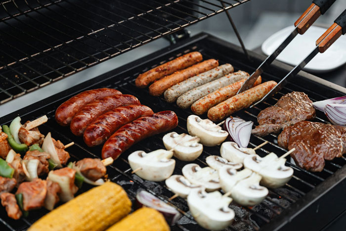 A family barbeque with sausages, corn, mushrooms, and onions on a grill. A family barbeque with sausages, corn, mushrooms, and onions on a grill.