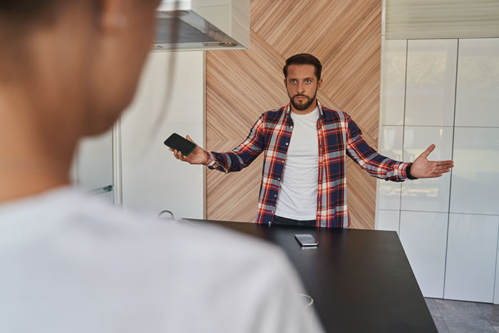 Man in plaid shirt gesturing in a kitchen, confronting a woman. Man in plaid shirt gesturing in a kitchen, confronting a woman.