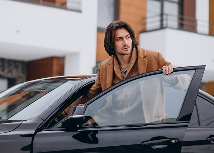 Man in a brown coat sitting in a black car during a yard sale event with police intervention.