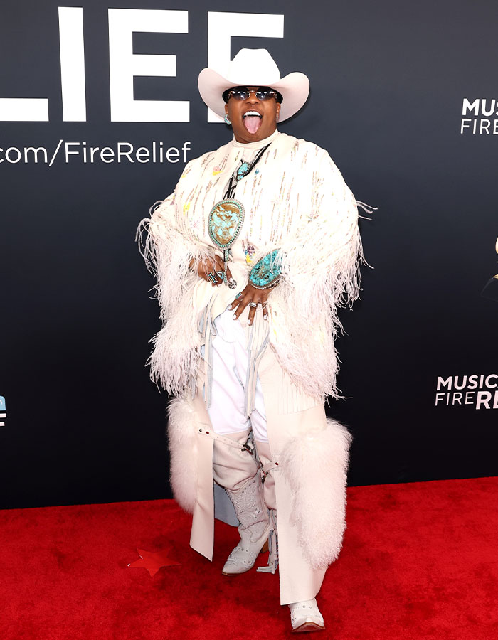 Celebrity in a white fringed outfit and cowboy hat on the red carpet at the 2025 Grammys.