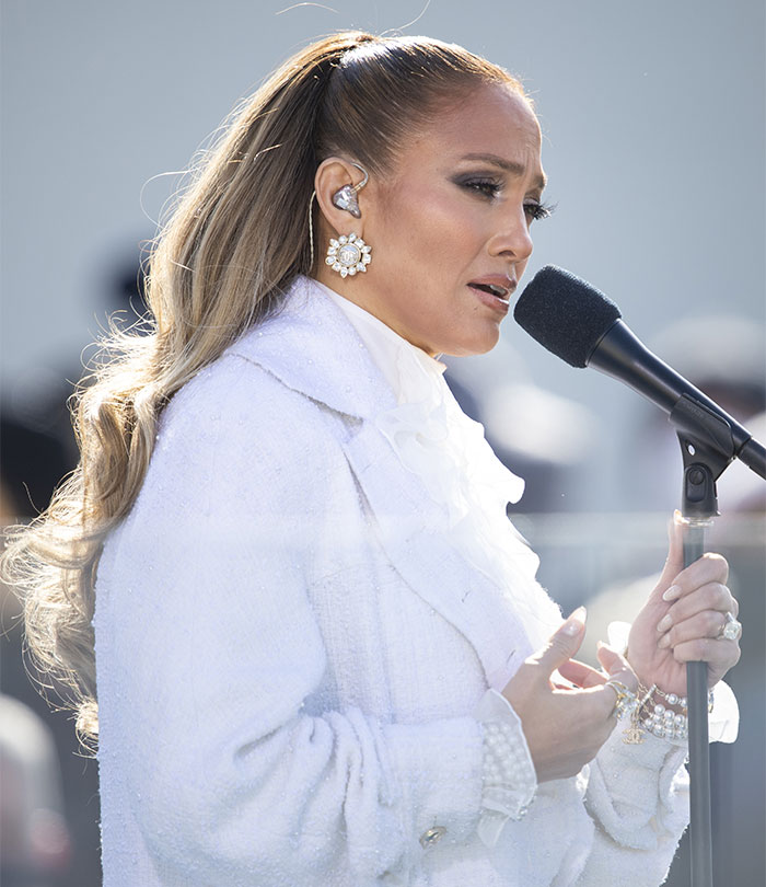 Singer performing outdoors, wearing a white coat and using a microphone.
