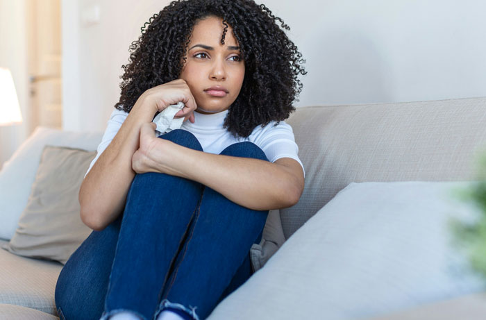 Woman sitting on a couch, looking contemplative after uncovering something crazy in a man's background.