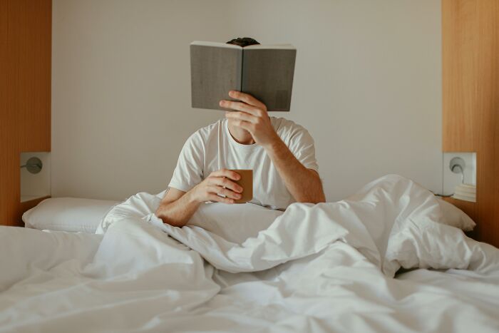 Man in bed reading a book and holding a cup, illustrating concepts related to things real men don't do.