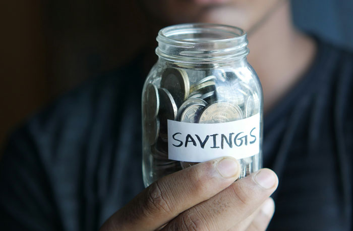 Person holding a jar labeled "savings," filled with coins, illustrating wealth perception.