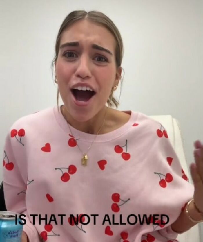 Woman expressing surprise in a pink sweater with cherries pattern, discussing an outfit considered inappropriate for work. Woman expressing surprise in a pink sweater with cherries pattern, discussing an outfit considered inappropriate for work.