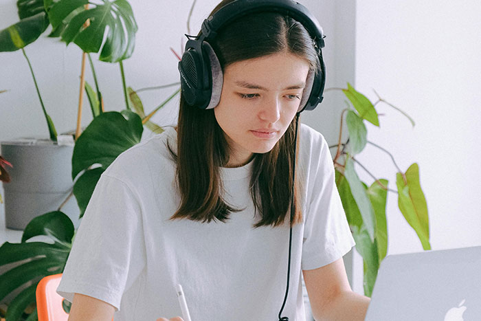 Woman wearing headphones, using a laptop to explore safe side hustle ideas at a desk with plants.