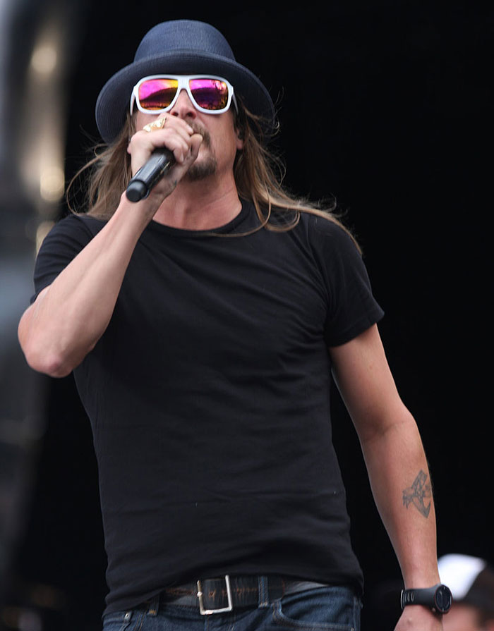 Singer on stage wearing sunglasses and a hat, holding a microphone.