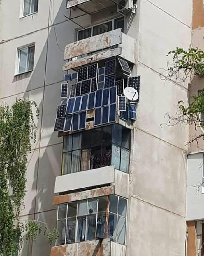 Paneles solares dispuestos de manera inusual en un balcón de edificio deteriorado.