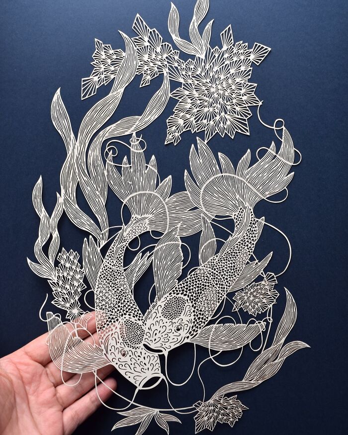 Intricate paper art design featuring nature-inspired patterns held by a person's hand against a dark background.