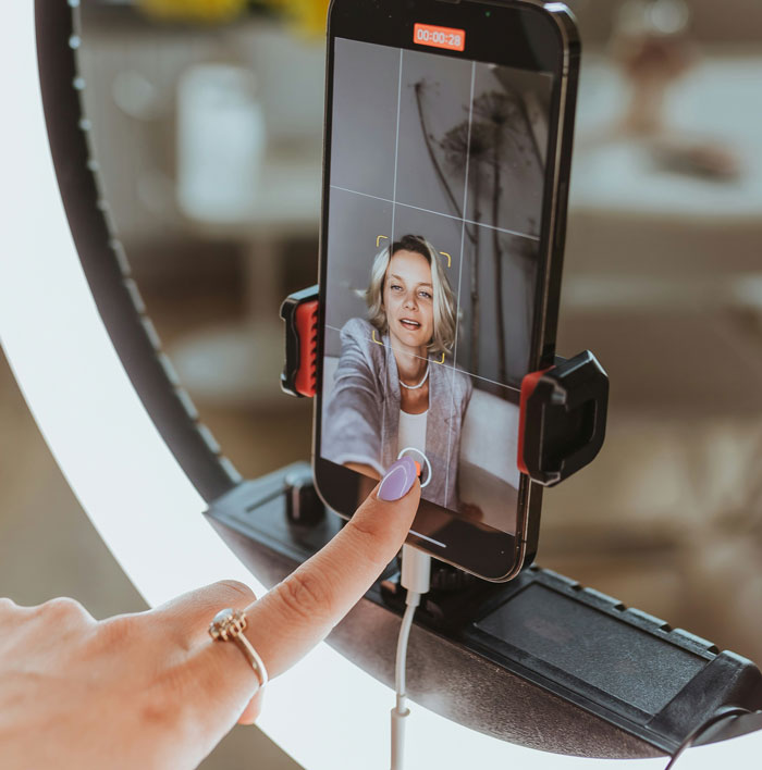 A woman takes a selfie with a ring light, capturing a live moment.