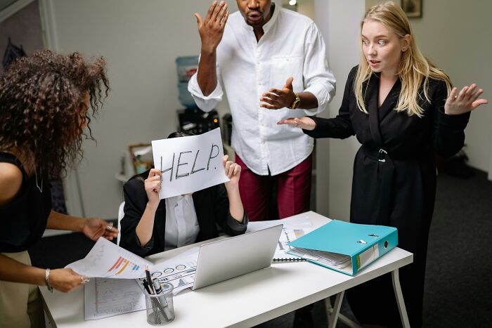 Group around a desk, one holding a "HELP" sign, embodying therapists' knowledge to change mindsets in a stressful setting.