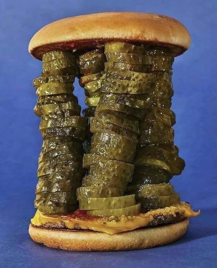A weird burger piled high with stacks of pickle slices against a blue background.