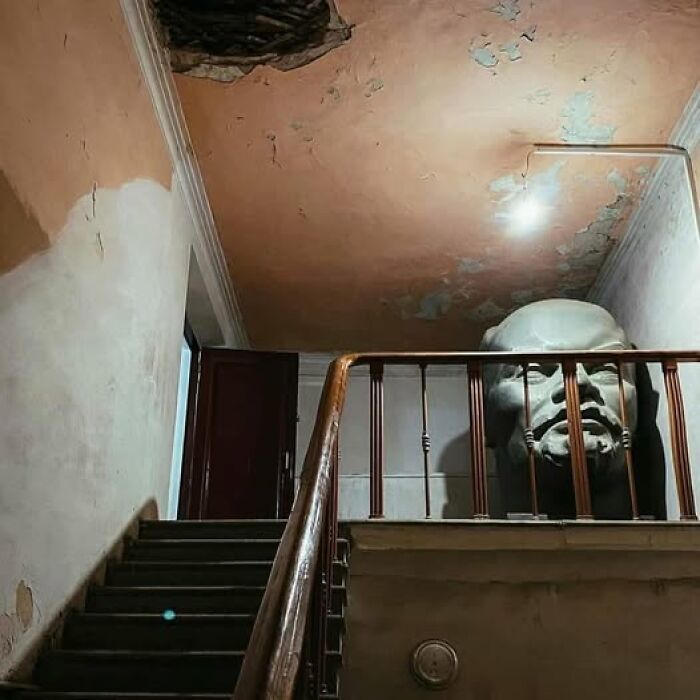 Escalera antigua con una estatua inusual detrás de una barandilla, destacando lo raro del lugar.