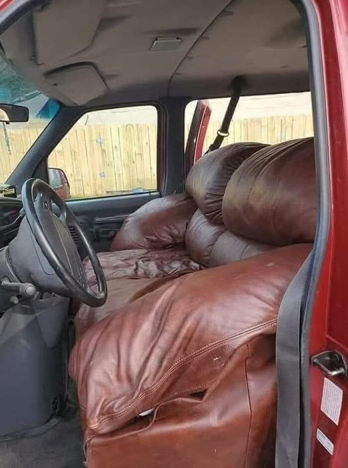 Red truck interior with a large brown couch replacing the front seats, showcasing a weird image worth seeing.