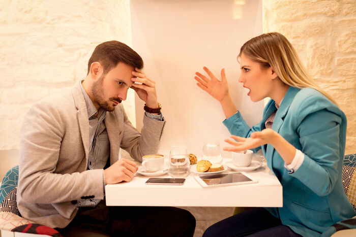 A man and woman arguing at a cafe table, showcasing non-physical qualities of unattractiveness.
