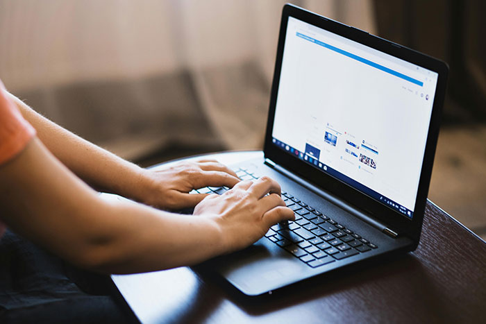 Person typing on a laptop, searching for safe side hustle ideas online.