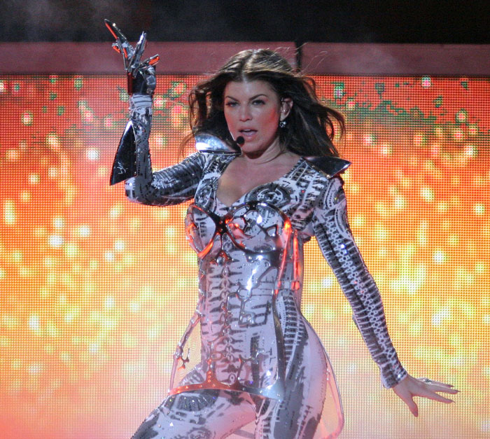 Singer performing energetically on stage in a futuristic silver outfit.
