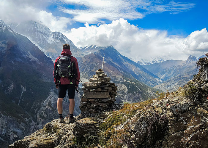 Hiker with backpack on mountain ledge, gazing at stunning range; a tranquil scene contrasting life and dying patients' last words.