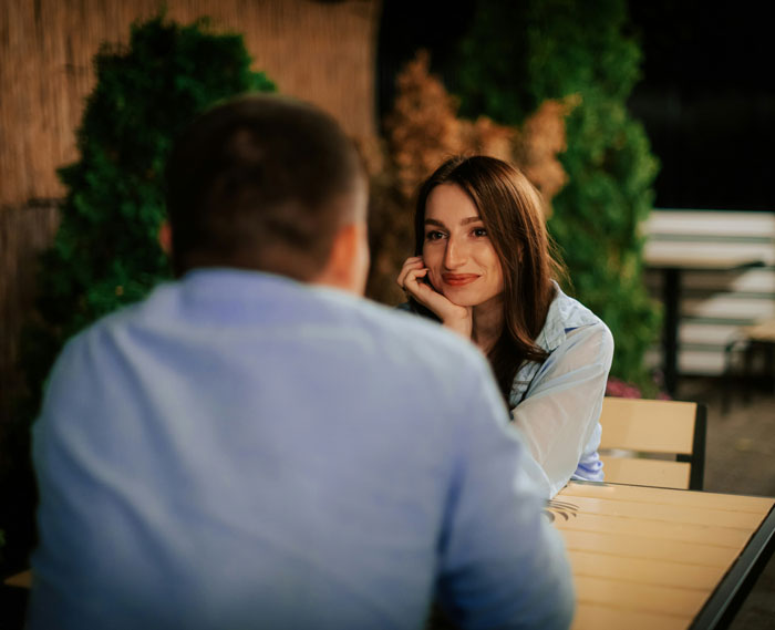 A woman smiling at a man during dinner outdoors, relating to uncovering background stories.