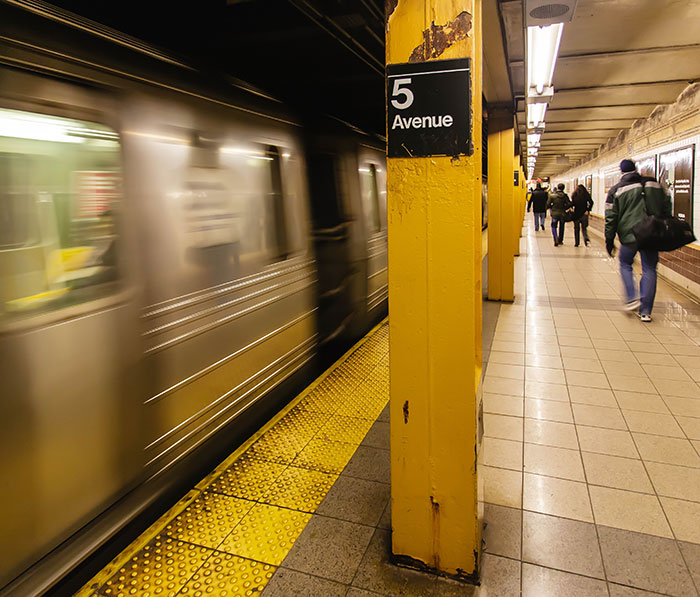 5th Avenue subway station in NYC at midnight, train arriving, few people on platform, dimly lit atmosphere.