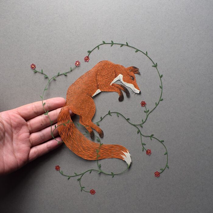 Intricate paper art design of a fox surrounded by floral patterns, held in hand.