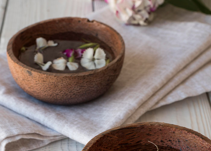 A rustic wooden bowl with a whimsical floral arrangement, placed on a light fabric.