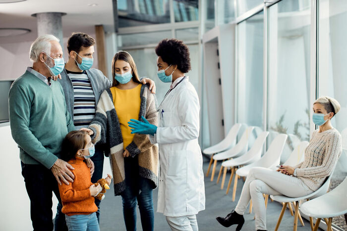 Family in masks speaking with a doctor, illustrating American norms around health and safety in a medical setting.